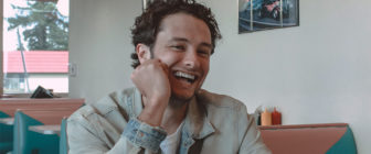 Man sitting at booth in restaurant leaning on one hand and laughing