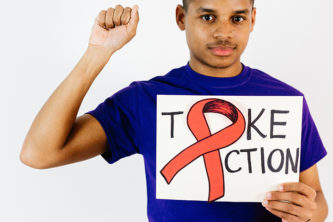 young man in indigo shirt holds sign with red ribbon that says "take action" while holding up right fist