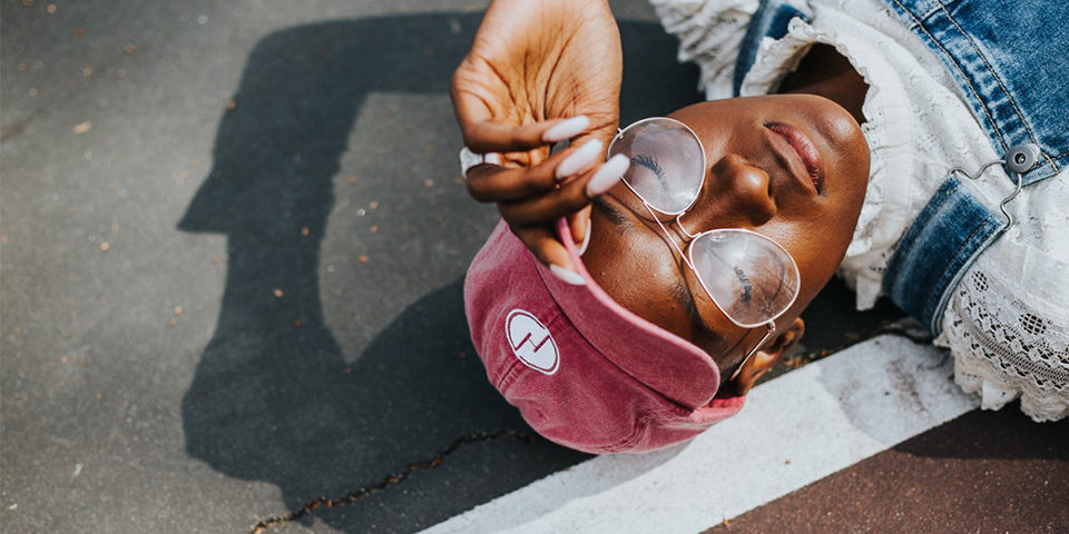 young woman with red hat and large glasses laying on pavement.