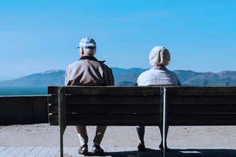older white couple sitting on park bench looking out at blue mountain scenery