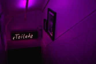 purple lights with neon sign that reads "toilets" over staircase