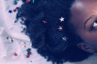 young black women lies on white background with confetti stars in her hair