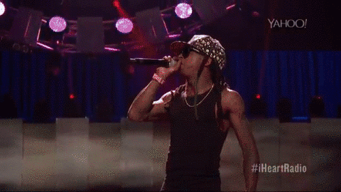 Lil Wayne singing and rapping in black tank top, camo snapback, and sunglasses