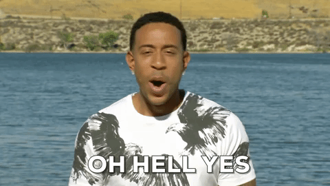 Ludacris in white and olive t-shirt standing in front of body of water with white text overlay: "OH HELL YES"