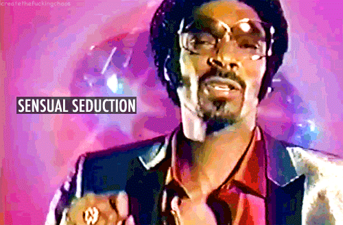 Snoop Dogg in black sports jacket and shiny red button-down dancing in front of a pink, white, and blue background. The gif is made to look like it's from the 70's.